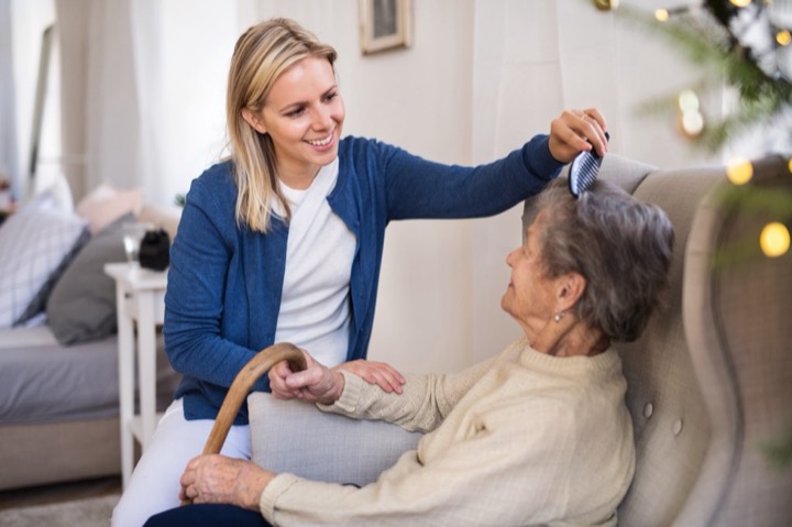 Younger woman caregiver brushing the hair of an elderly woman sitting in a comfy chair