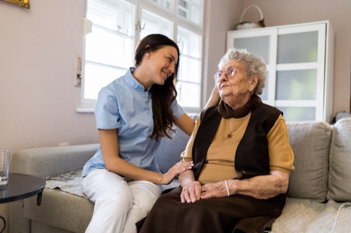 Smiling woman caregiver sitting next to and looking at happy senior woman on a couch