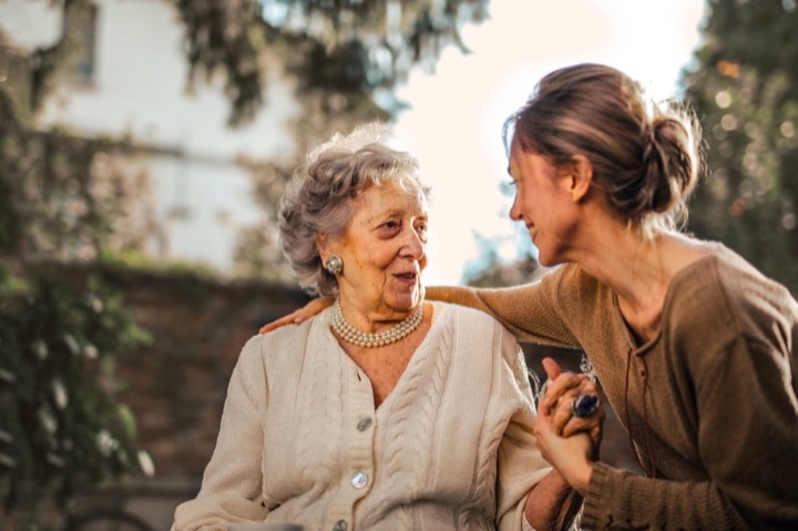 Elderly lady and middle aged caregiver smiling, talking and holding hands